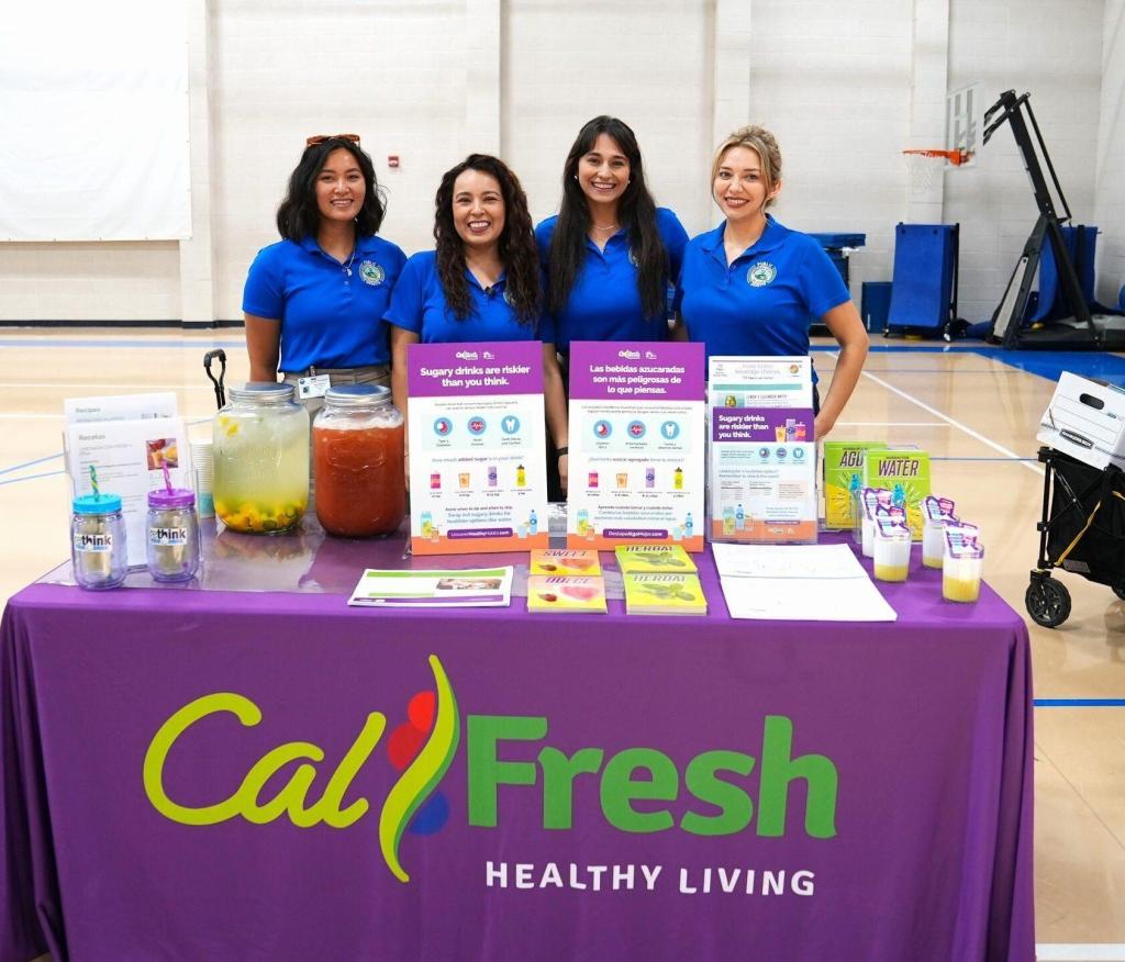 A group of women pose behind a booth that reads calfresh healthy living.