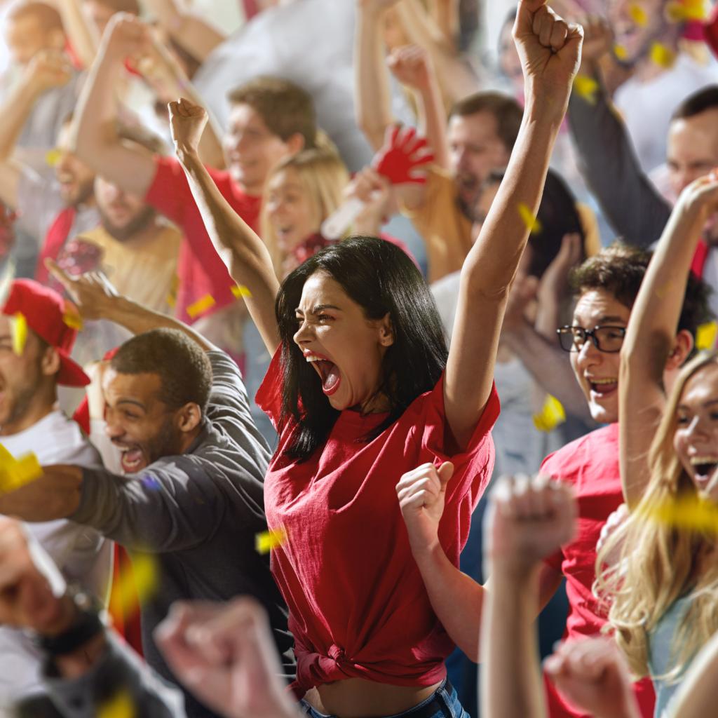 A lady in a red t-shirt is cheering in packed sports team stadium.