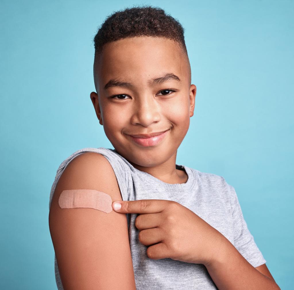 Happy child points to band aid on arm with joyful smile