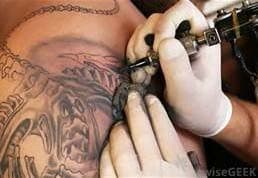 close up of tattoo artist wearing white gloves mid-way through drawing complex design on person's shoulder