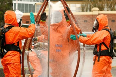 three people in orange hazmat suit outside with hands in the air getting washed off with water