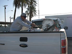 Public health vector control employee wearing a cap and grey jacket operating machinery on the back of white truck.