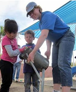 female Public Health employee assisting two young children ,girl and boy, water a garden